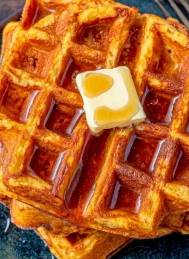 Delicious French toast waffles drizzled with syrup and topped with fresh berries