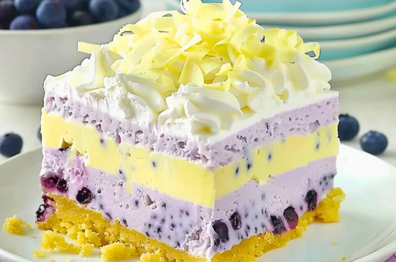 A vibrant slice of lemon blueberry lasagna topped with fresh blueberries and lemon zest.