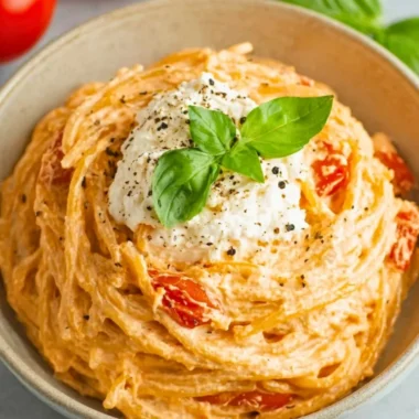 Bowl of roasted tomato and garlic ricotta pasta garnished with fresh herbs