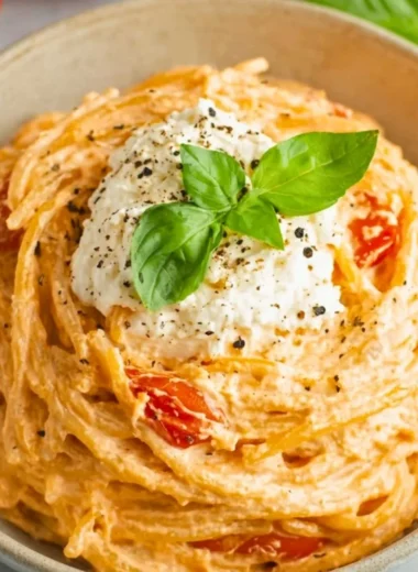 Bowl of roasted tomato and garlic ricotta pasta garnished with fresh herbs