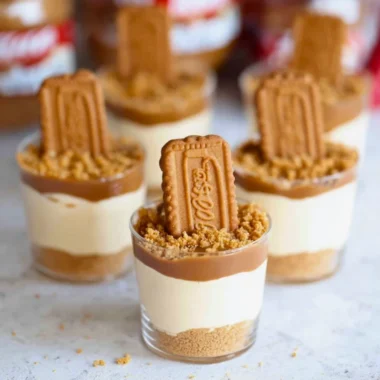 No Bake Biscoff Cheesecake Cups topped with caramel drizzle and cookie crumbles