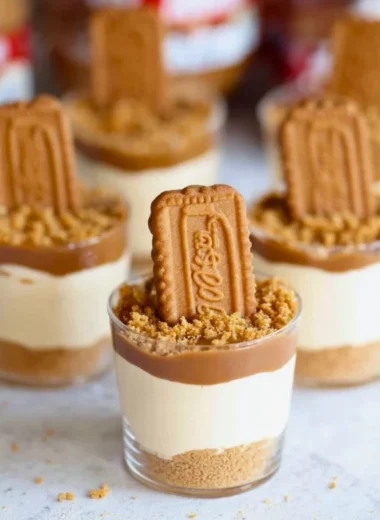 No Bake Biscoff Cheesecake Cups topped with caramel drizzle and cookie crumbles