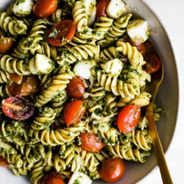 Colorful bowl of Pesto Pasta Salad topped with cherry tomatoes and basil.