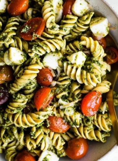 Colorful bowl of Pesto Pasta Salad topped with cherry tomatoes and basil.